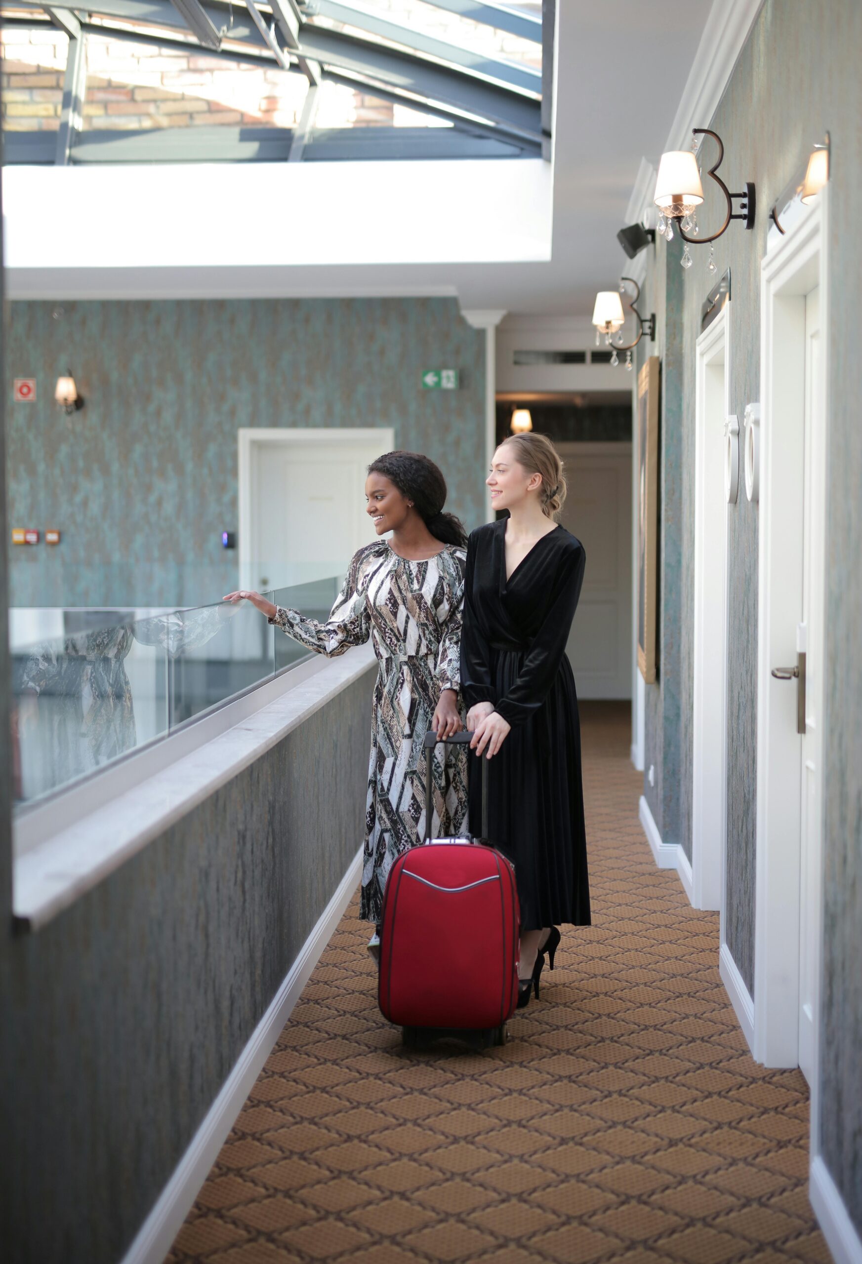 Two fashionable women with luggage in a stylish hotel hallway.
